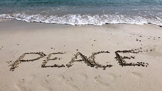 Bild på sandstrand där någon skrivit "Peace" i sanden. Illustrerar freds- och konfliktstudier.
