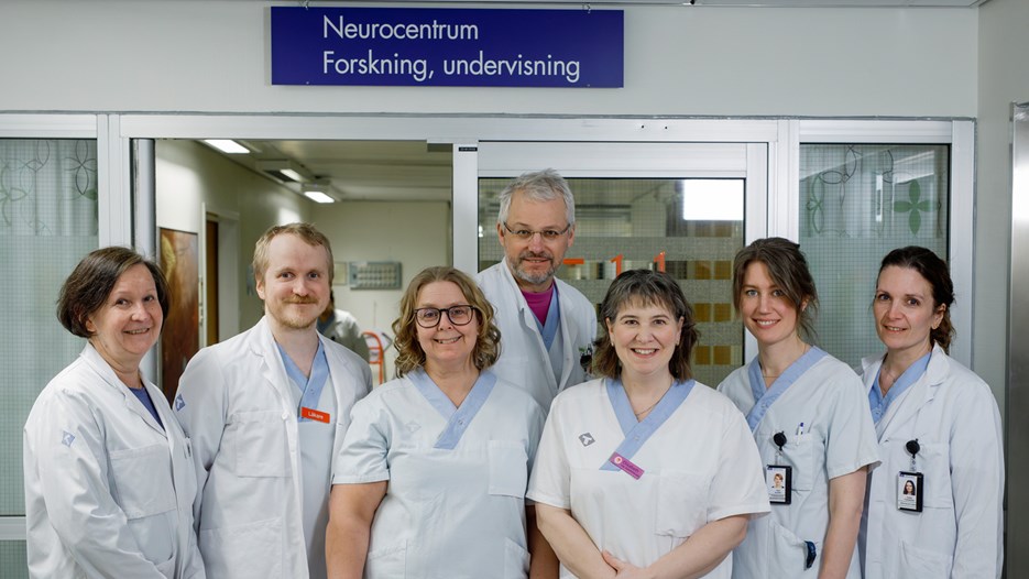 Gruppbild på Lena Bylund, Ivar Winroth, Nina Sundqvist, Peter Andersen, Elisabeth Müller Granberg, Tina Björn och Karin Forsberg som står utanför Neurologens forskningsavdelning och tittar in i kameran. På en skylt ovanför dörren står Neurocentrum Forskning, undervisning. 