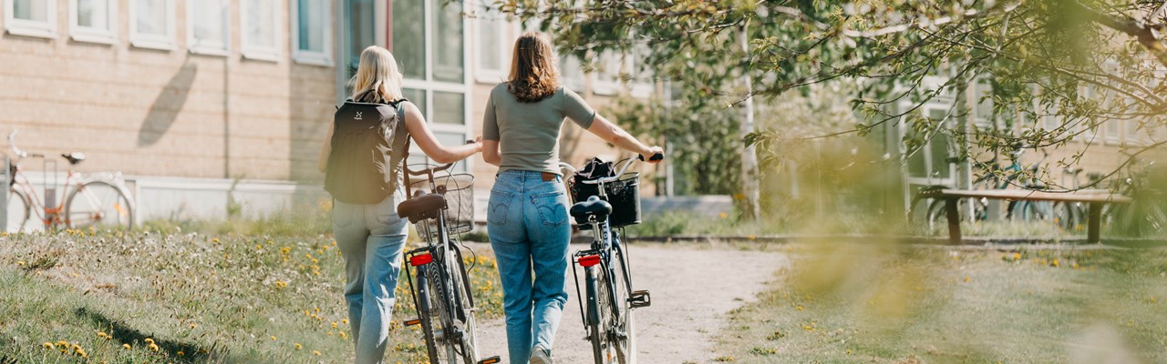 Två kvinnor går och leder varsin cykel på en grusväg.