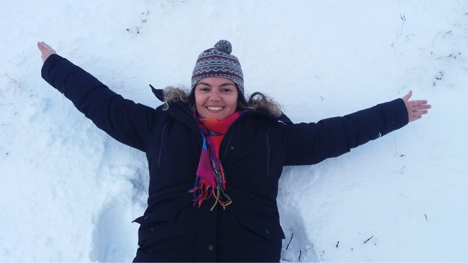 International student laying in the snow wearing a hat and scarf