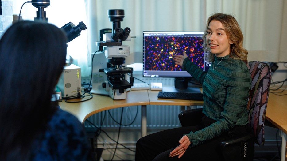 Isabelle Sigfridsson sitter i fluorescensmikroskoprummet och visar en kollega resultatet från en multiplexinfärgning som syns på en datorskärm.