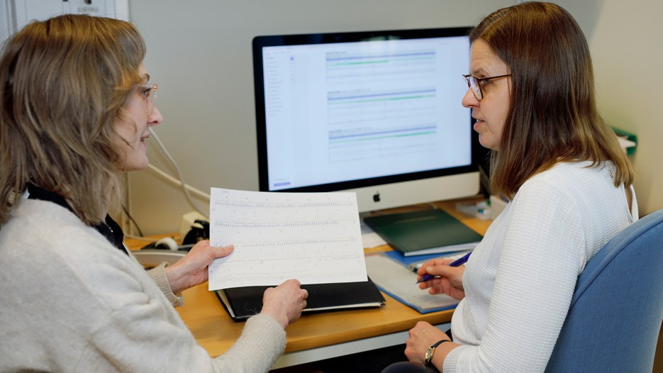 Eva Jonsson is sitting at her desk infront of a computer screen. Angelica Nordin is sitting next to her, holding a print-out of sequencing data that they are discussing.