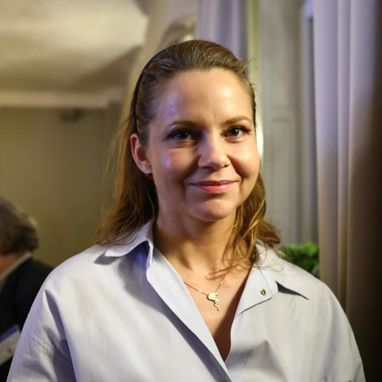 En kvinna som står i ett rum med människor i bakgrunden.