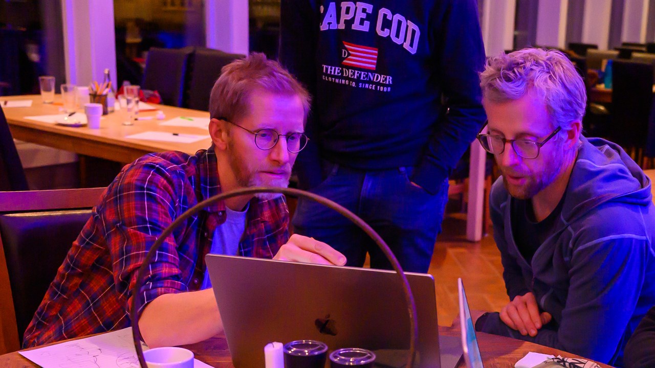 Three people sitting and one standing looking at a laptop