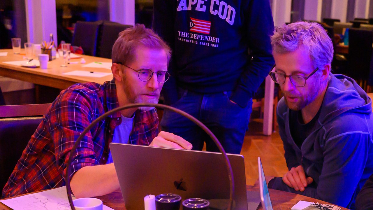 Three people sitting and one standing looking at a laptop