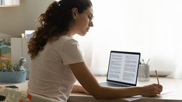 En student sitter hemma och skriver en hemtenta på sin laptop.