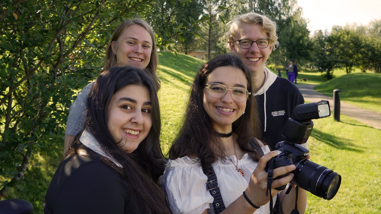 Fyra blivande studenter i datavetenskap väljer vilken bild de vill ha på sig själva. De står utomhus i solen och en av dem håller i kameran.