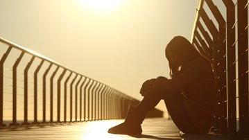 Sad teenager girl depressed sitting in a bridge at sunset