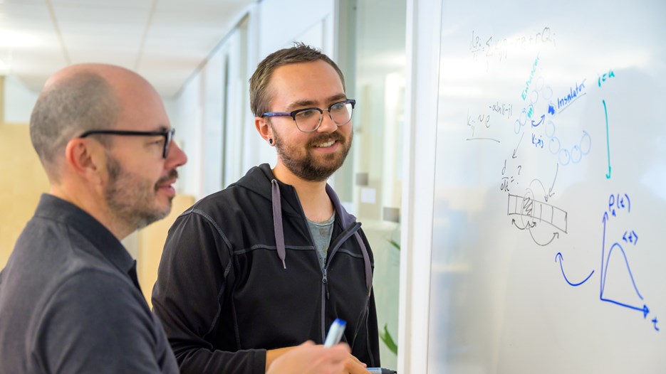 Two men look at drawings on a whiteboard