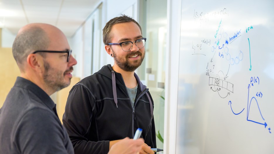 Two men look at drawings on a whiteboard