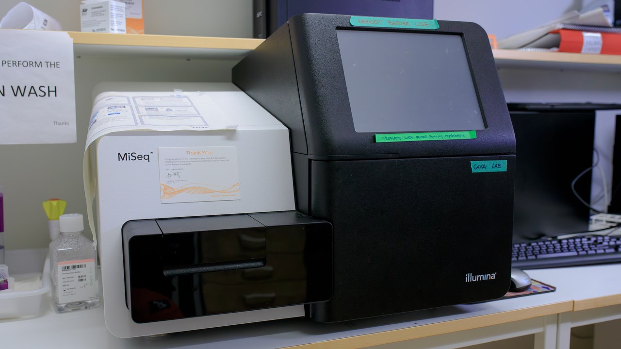 Bild på MiSeq-instrument för sekvensering som står på en bänk i ett labb. / Image of the MiSeq benchtop sequencing system equipment in a lab.