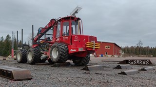 En skogsmaskin kör över hinder på en grusplan.