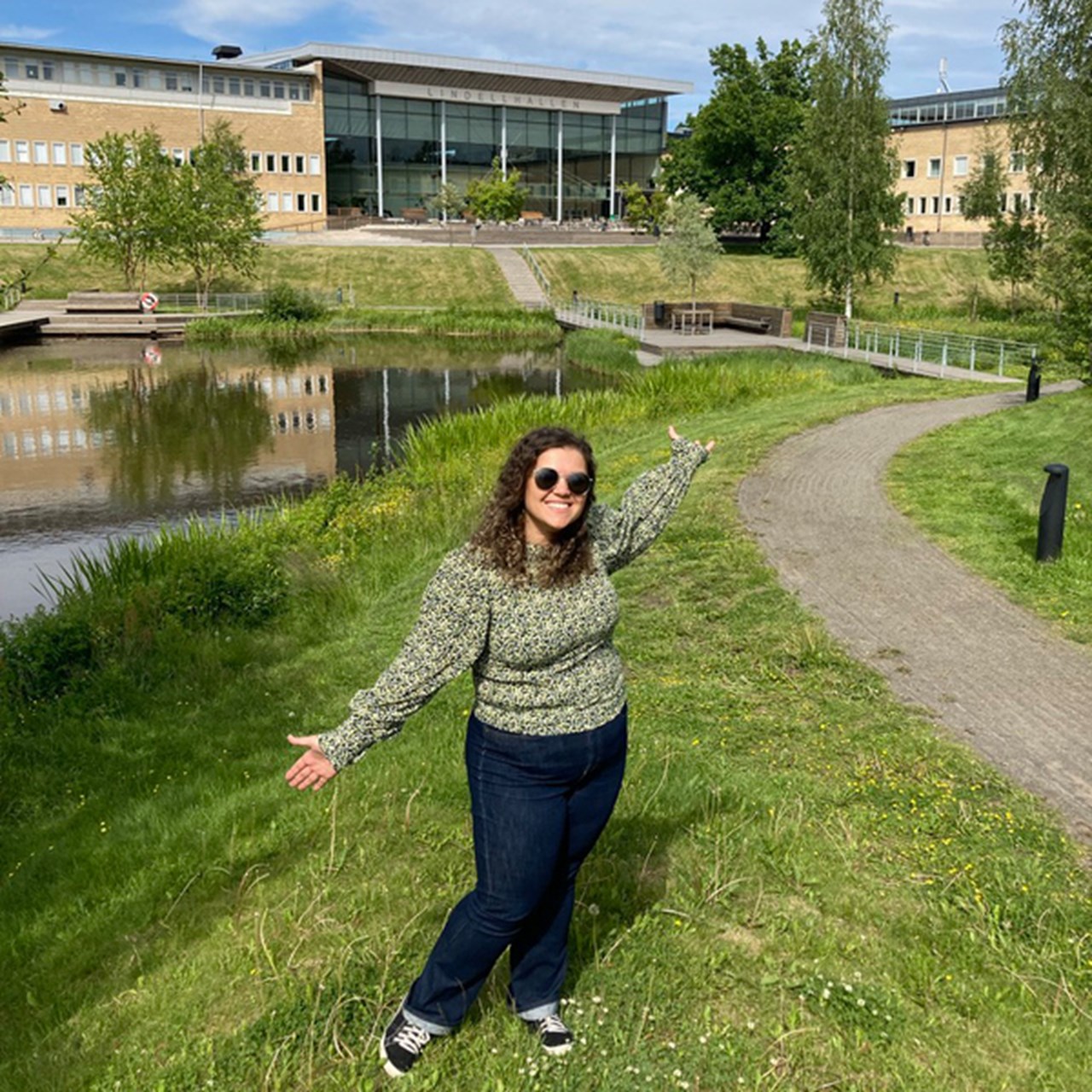 International student from Brazil posing in front of the campus pond at Umeå University