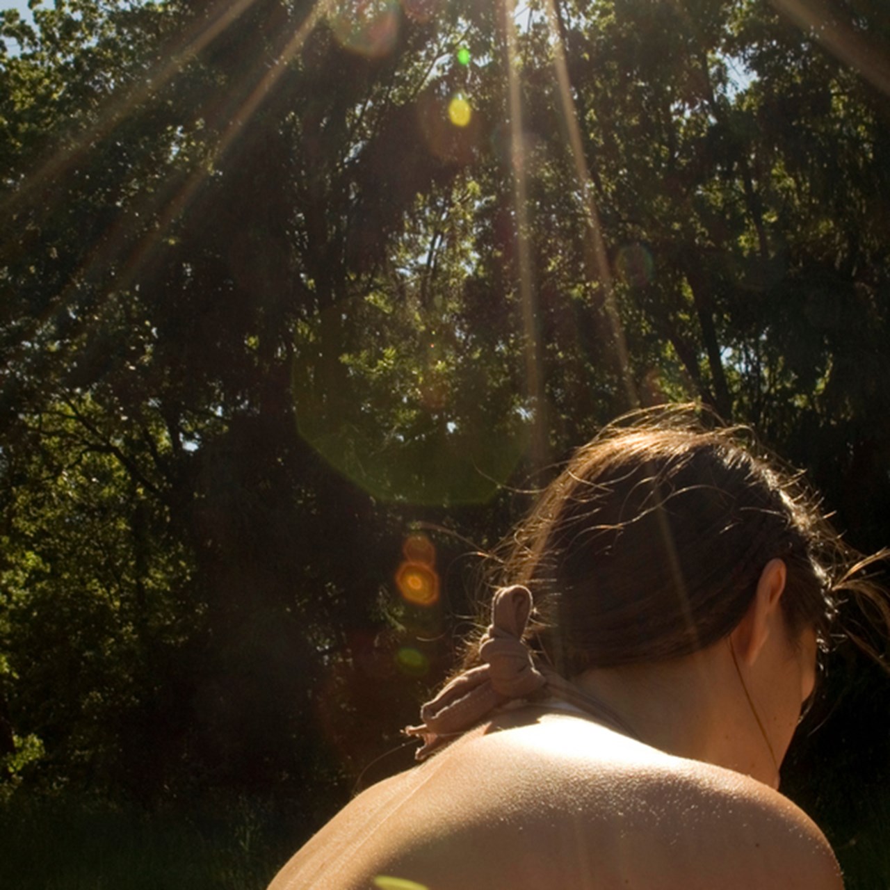 Kvinna sitter med bar hud under strålande sol. Skog i bakgrunden.