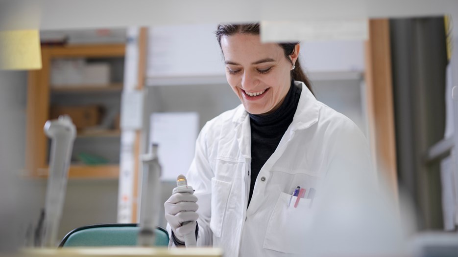 The PhD-student Caitlin Henne is seen pipetting samples at her lab bench smiling. 