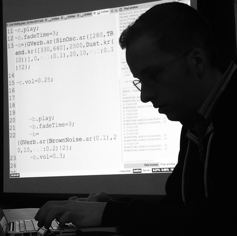 A man sitting in front of a laptop computer with code projected in the background