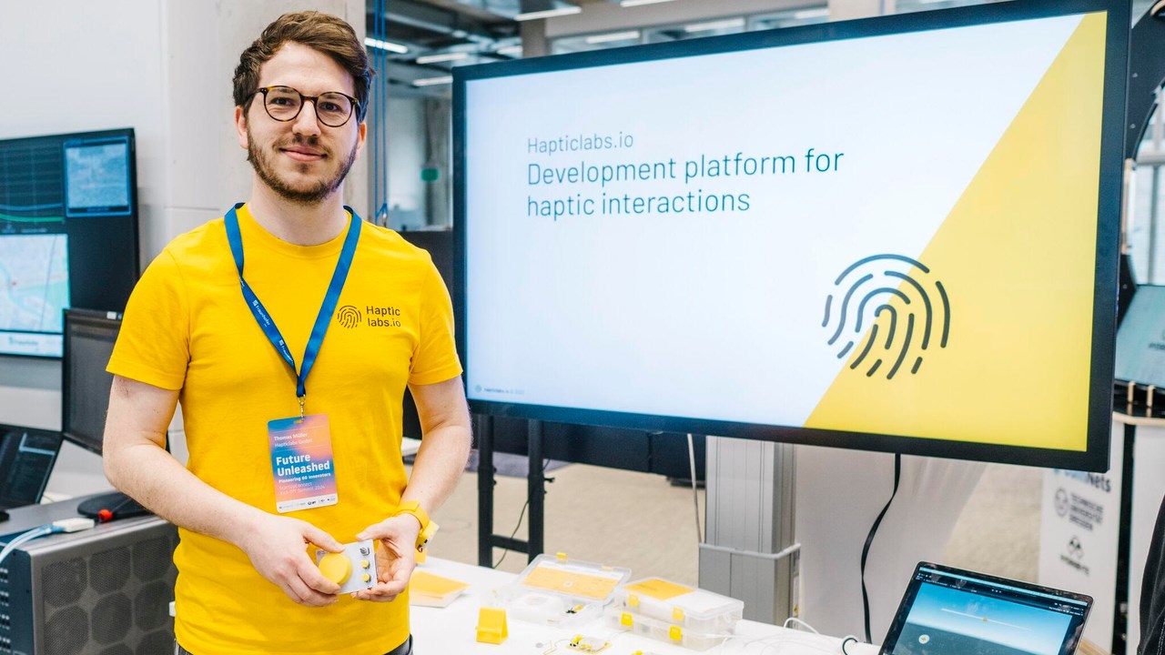 Bild på Thomas Müller i gul t-shirt stående framför en datorskärm med företaget Hapticlabs logotyp