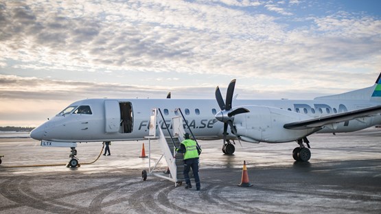 Ett flygplan som står på landningsplattan på Umeå flygplats. En flygplatsanställd håller på att ansluta trappan för att passagerare ska kunna gå ur planet.