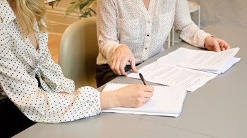 Två kvinnor sitter vid ett bord och går igenom en rapport.