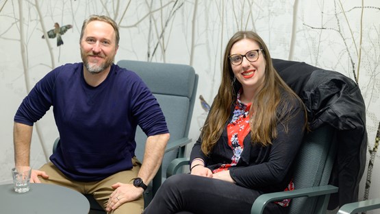 Eric Libby and Laura Carroll sit in IceLab against a background wallpaper of birds