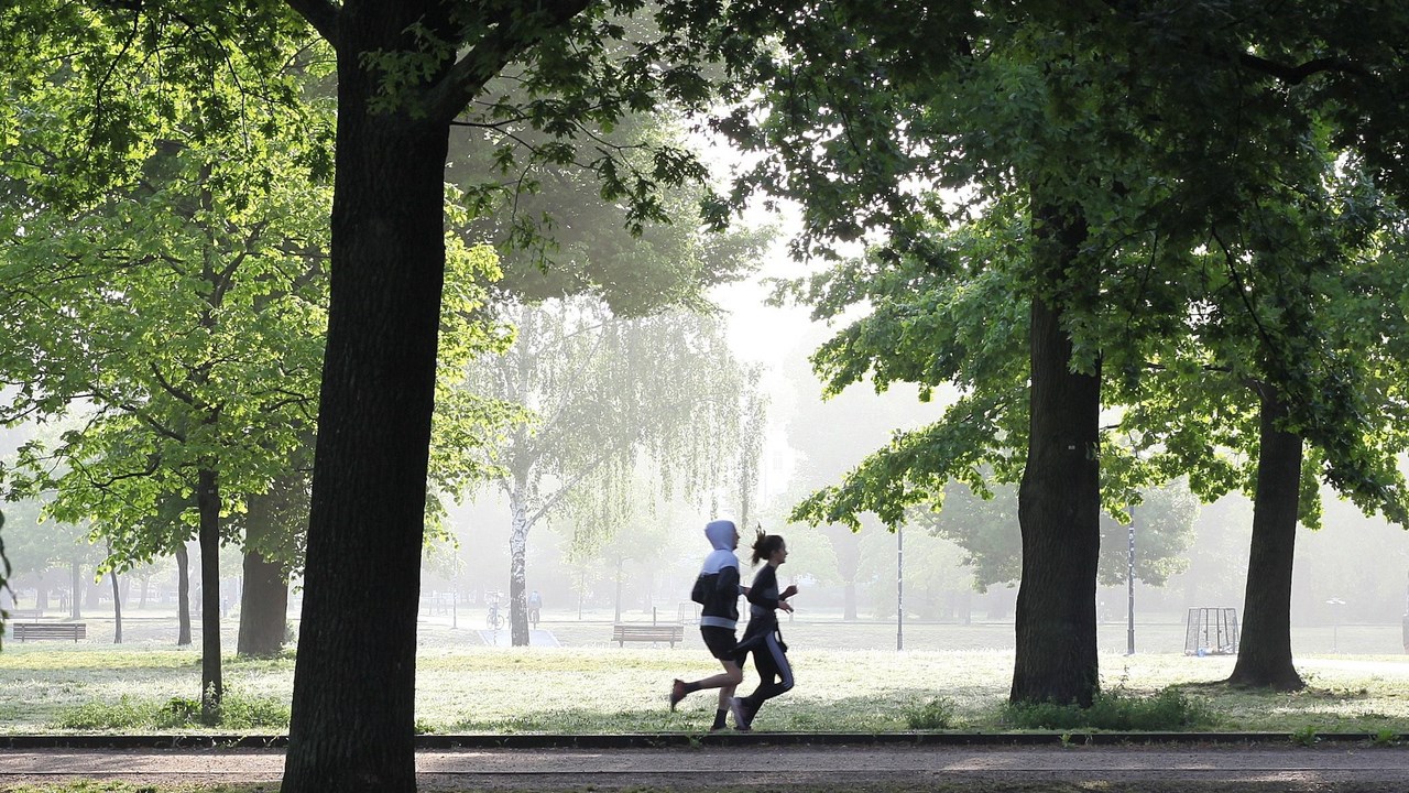 Man och kvinna springer i park i stadsmiljö