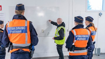 Polislärare Conny Tärnklev instruerar polisstudenter vid vita tavlan i Polisutbildningshusets garage.