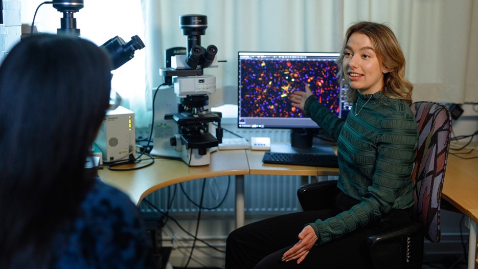 Isabelle Sigfridsson is sitting in the fluorescence microscopy room showing a colleague images on a computer screen seen behind her on the desk.