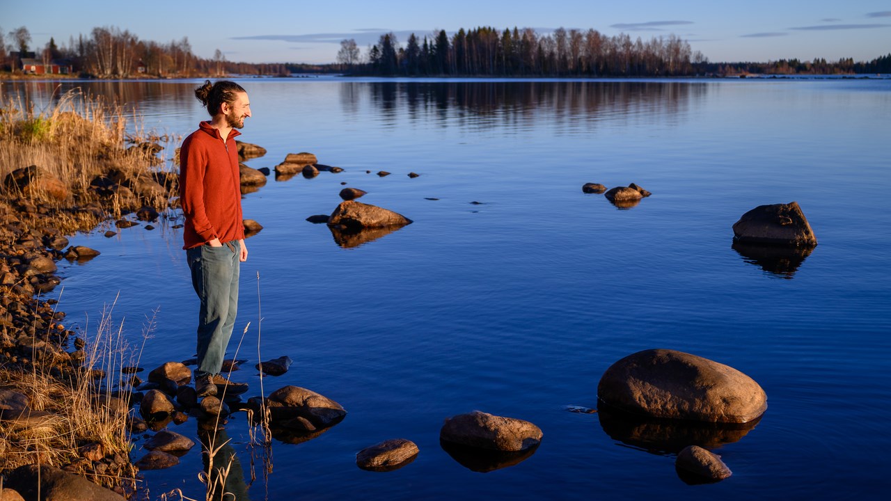 A man standing on a rocky shore next to a body of water