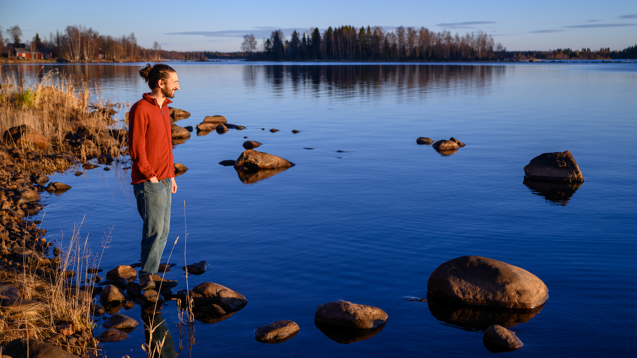 A man standing on a rocky shore next to a body of water