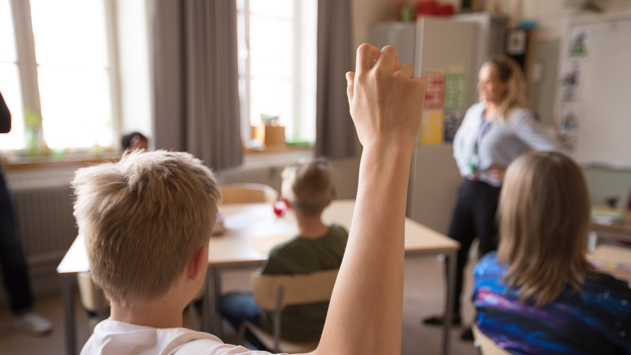 Mellanstadiebarn i klassrum. Pojke räcker upp handen.