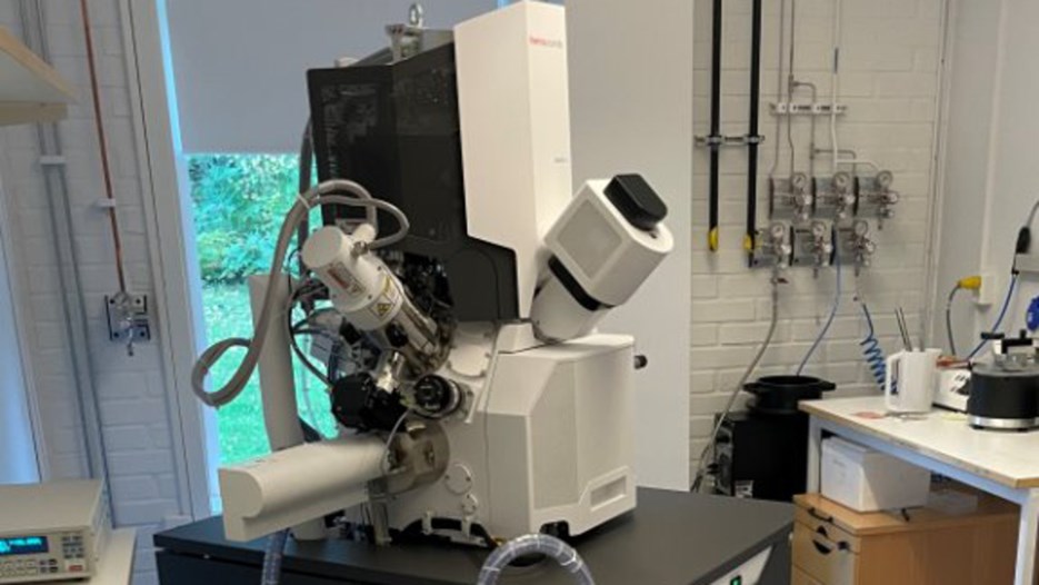 A large, 1x1x2 meter microscope. It is white and black, and connected with electric cables in a lab.