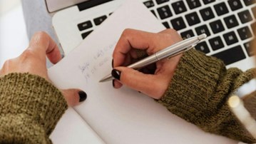 Händer som skriver på ett papper vid sin dator