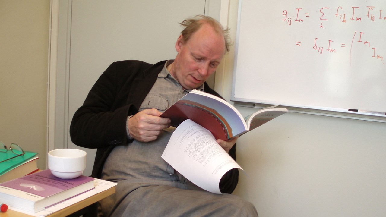 Bild av professor Roland Häggkvist som sitter på en stol och läser en tidsskrift