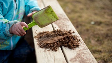 Detalj på barn på förskola som lägger upp sand med spade på kanten till sandlåda.