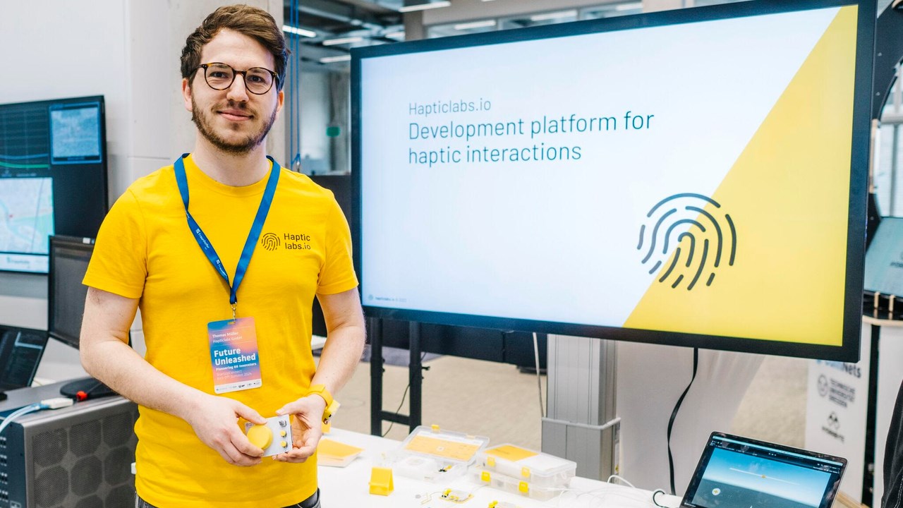 Thomas Müller wearing yellow t-shirt and standing in front of a screen with Hapticlabs logo.