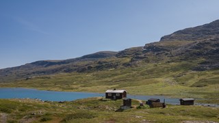 Vy över fjällandskap med några hus, en sjö och berget.