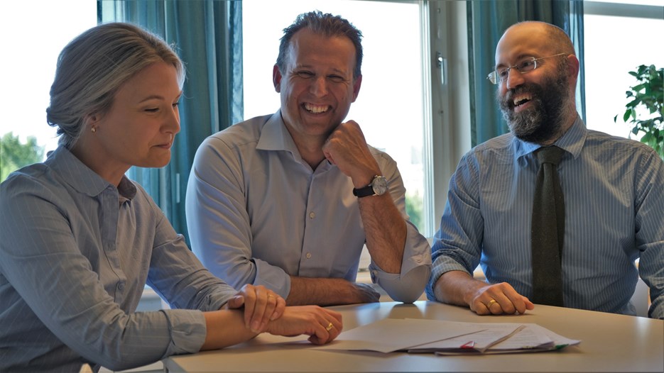 Therese Enarsson, Johan Holm och Jan Leidö sitter i möte vid ett bord, alla ler.  