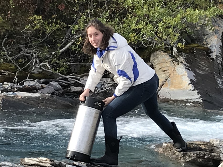 Emma Shipley stands over a stream with a test tube in her hands