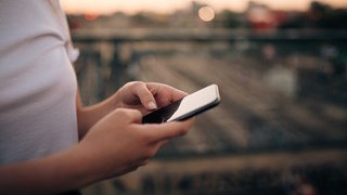 Woman holding a mobile phone in her hands seen from the side.