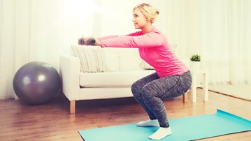 Kvinna gör övning på yogamatta hemma i sitt vardagsrum.