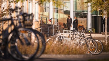 Några personer står och pratar utomhus på campus. Höstfärger i bekgrunden.