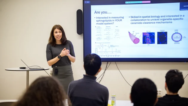 Elin Chorell stands by a screen displaying a slide outlining her need for collaborators.