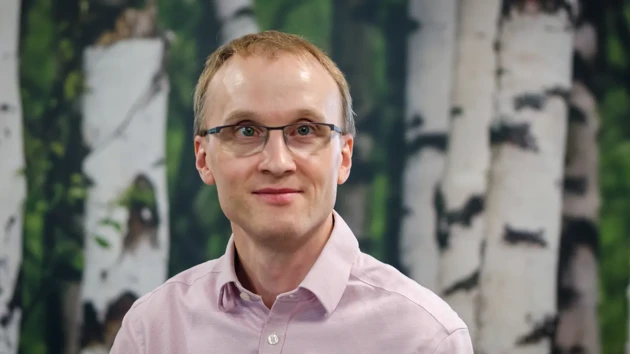 A man wearing glasses standing in front of a painting