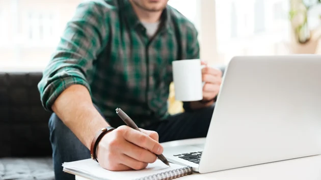 Man med kaffekopp arbetar framför en laptop.