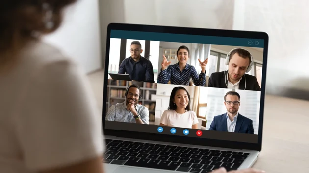 A person in the foreground at a computer with an open Teams meeting.