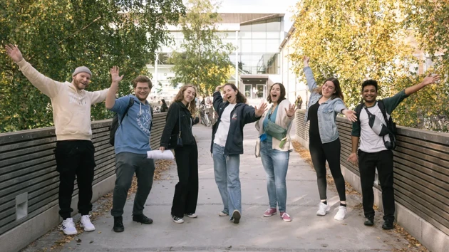 Seven students stand on a path with their arms raised in the air.