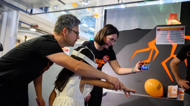 A man and a woman guide a child in a white dress with a white VR headset on