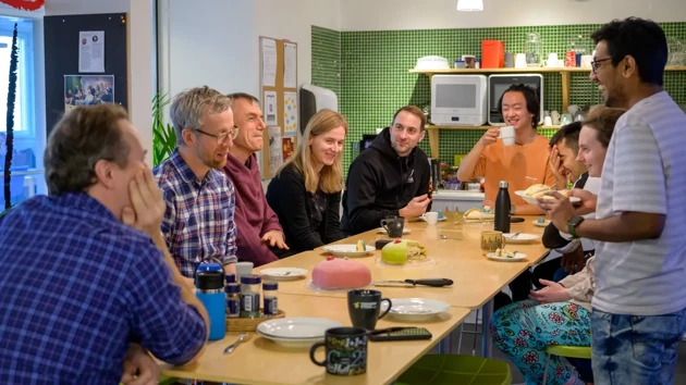 A group of people sitting around a wooden table sharing cake and talking