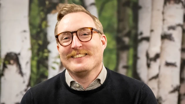 A man with glasses and a mustache standing in front of a painting