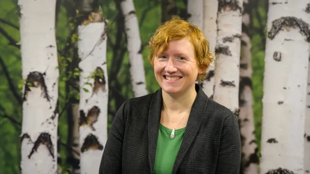 A woman standing in front of a painting of trees